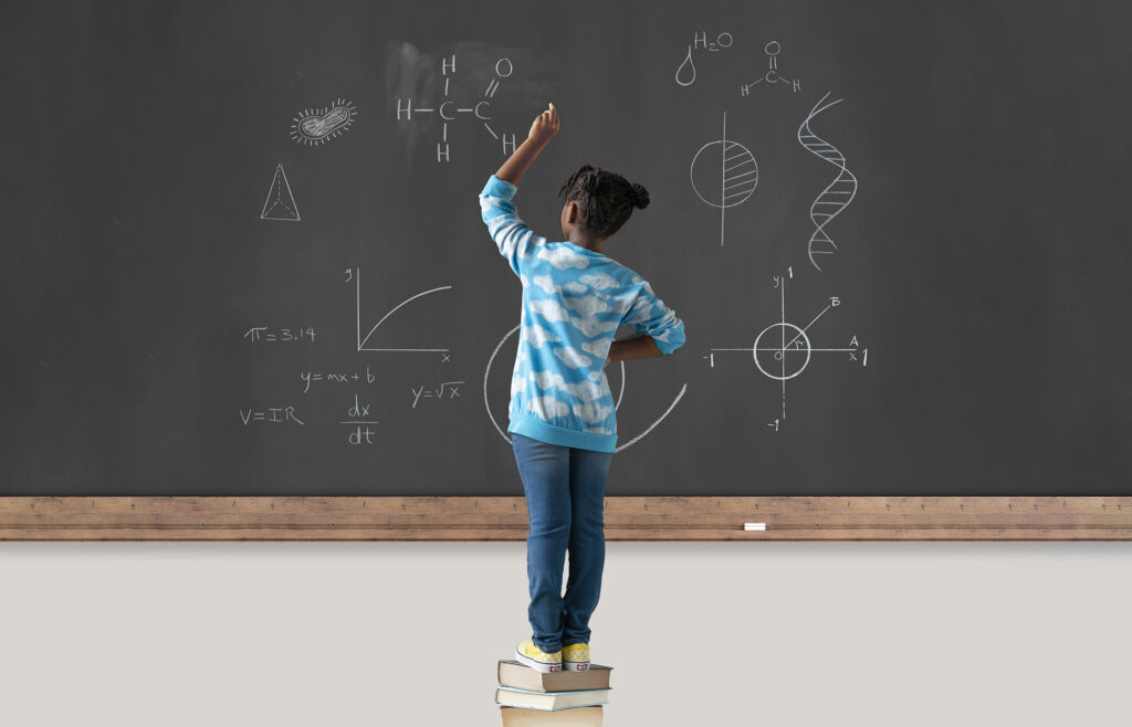 child at blackboard standing on books