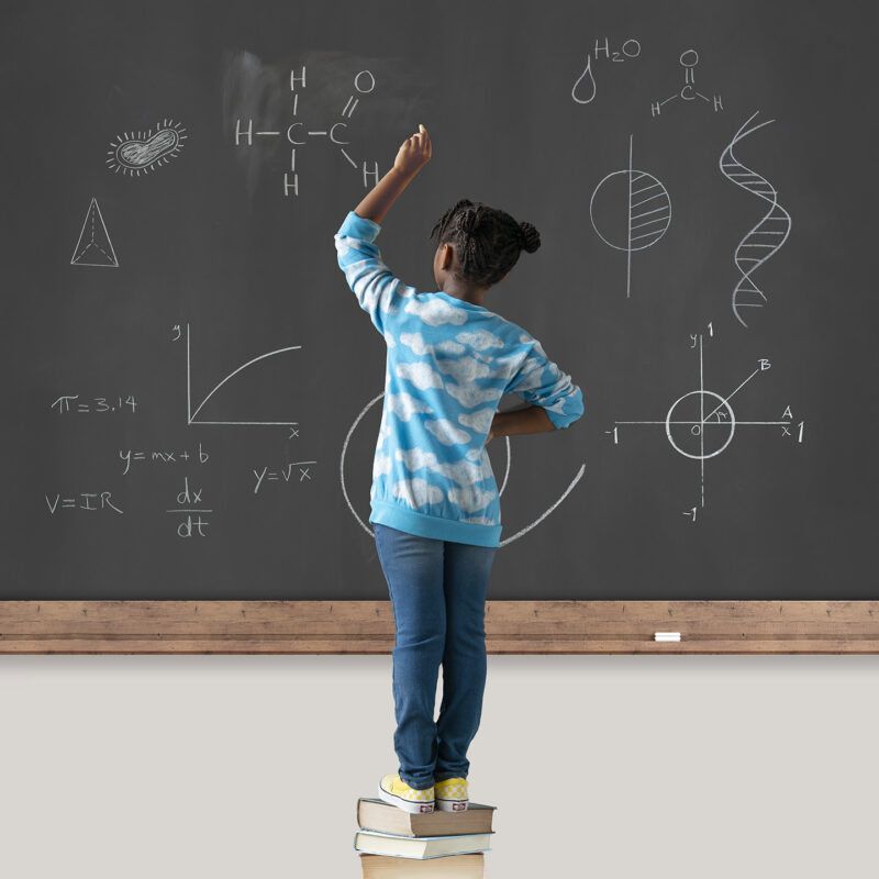 child at blackboard standing on books