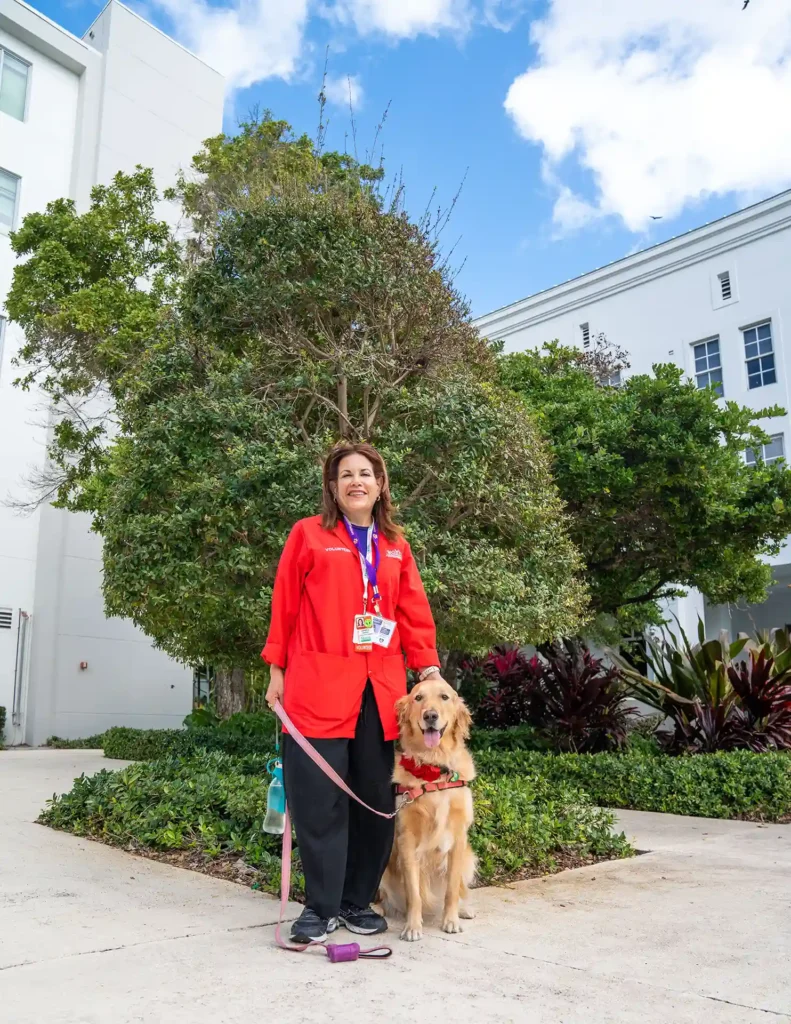 smiling golden retriever with handler in front of tree on campus